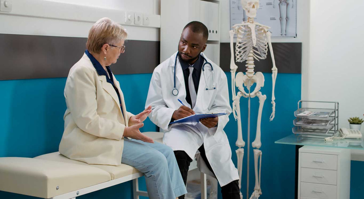 A doctor and a patient talk in an exam room next to a medical skeleton