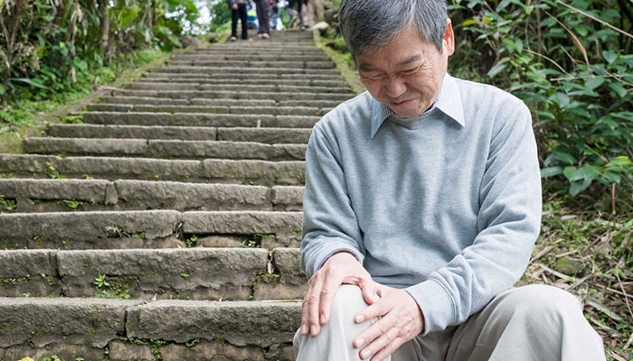An older man with knee pain, sitting on steps