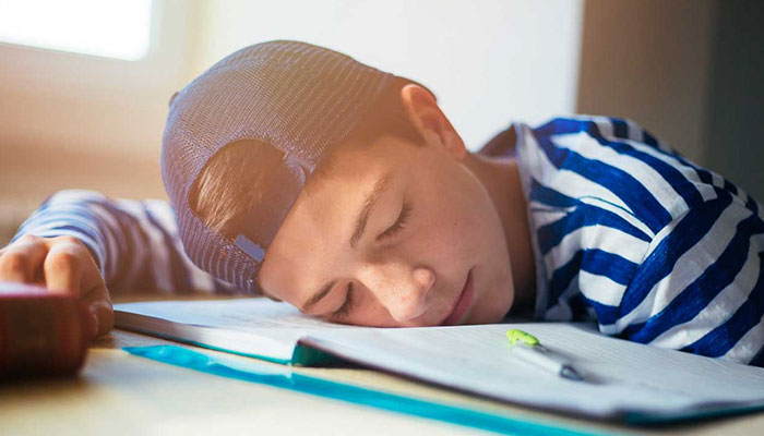 A teen sleeps on a textbook